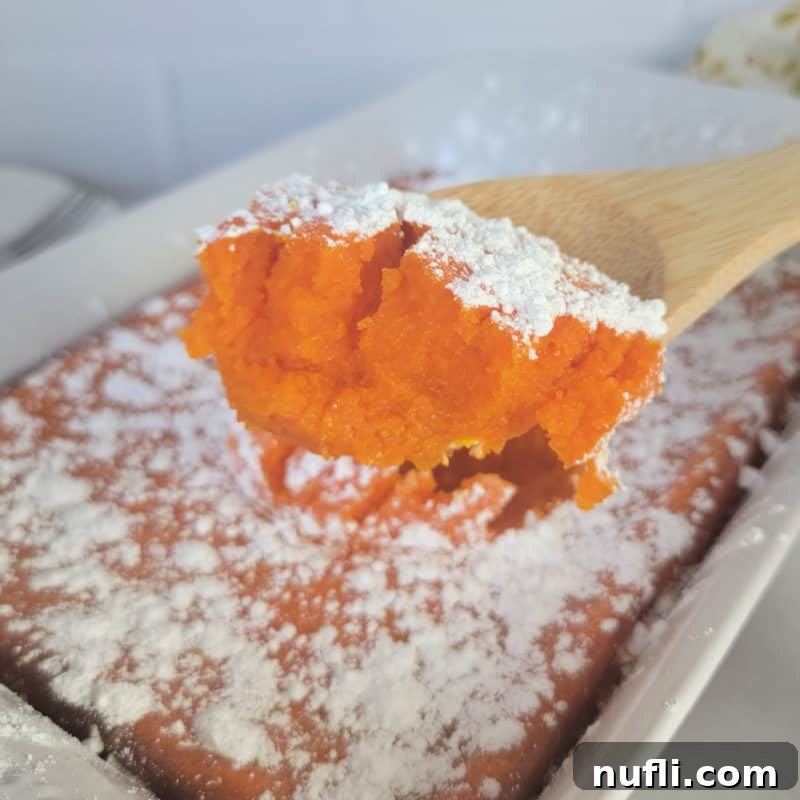 carrot souffle with powdered sugar garnish on a wooden spoon above a white casserole dish