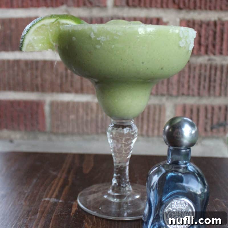 Avocado Margarita with a lime wedge next to a small bottle