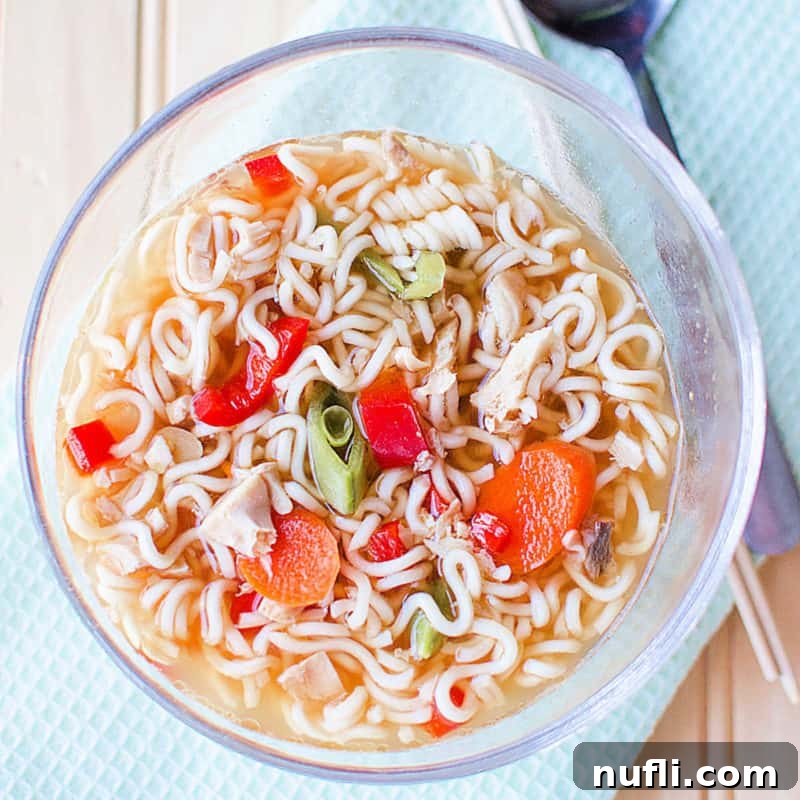 A comforting bowl of Chicken Ramen Soup in a clear glass bowl, served next to a spoon, inviting warmth and flavor.