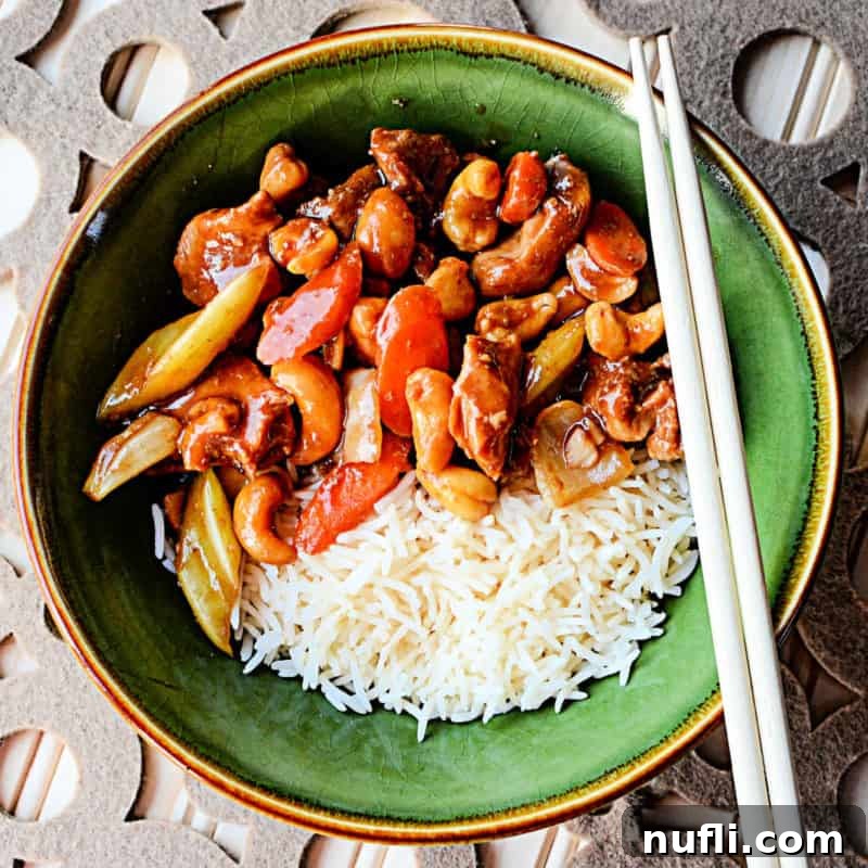A vibrant bowl of Cashew Chicken next to white rice, served in a green bowl with chopsticks, ready to be enjoyed.