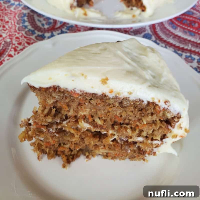 A decadent slice of Carrot Cake with Pineapple, Coconut, and Port Wine, adorned with creamy cream cheese frosting, served on a white plate.