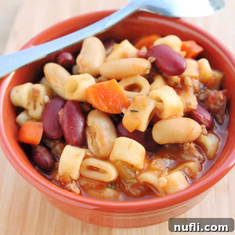 A rich orange bowl filled with beans and small round pasta, preparing for a comforting pasta e fagioli soup.
