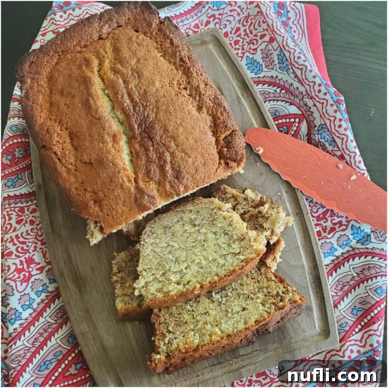 Loaf of sour cream banana bread with slices cut on a wooden cutting board with knife and cloth napkin