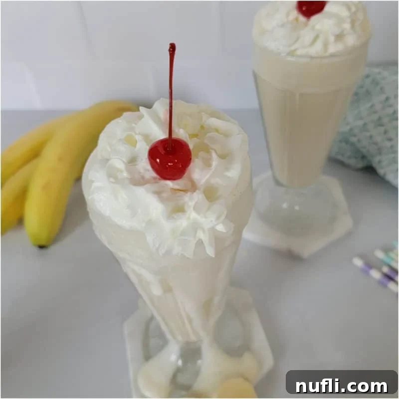 Banana milkshake with whipped cream and a cherry next to bananas and paper straws