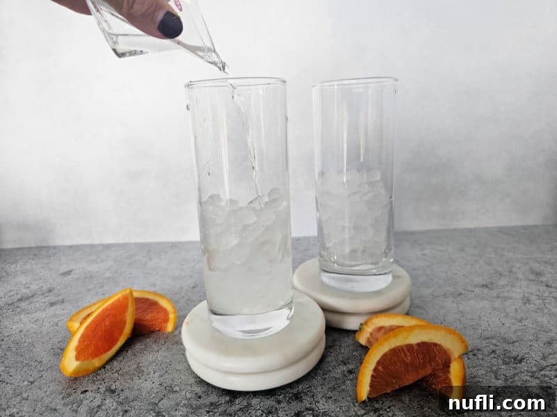 Vodka pouring over ice in a tall glass for a vodka sunrise drink