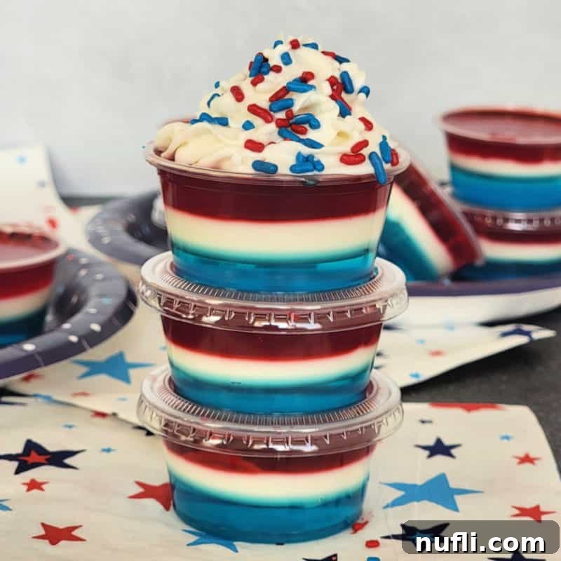 Vibrant red, white, and blue jello shots neatly arranged in plastic cups on star-themed napkins.