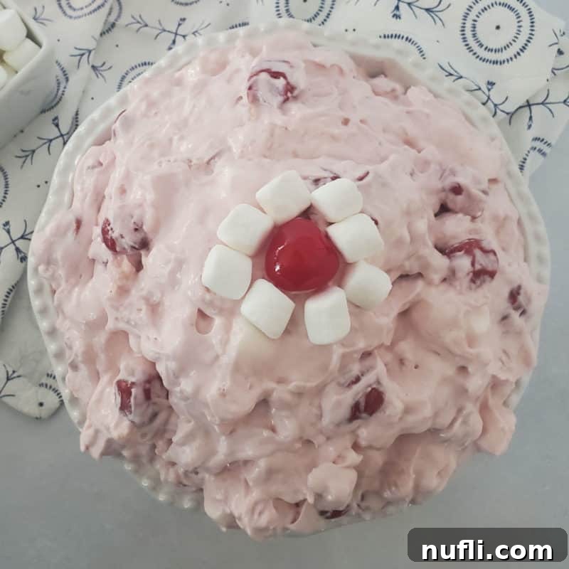 Cherry fluff salad in a white bowl garnished with mini marshmallows and a maraschino cherry