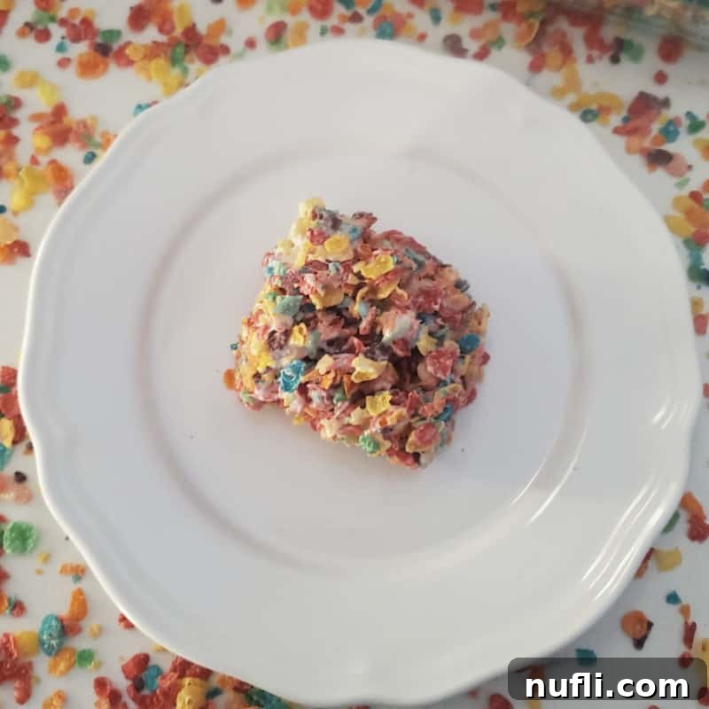 Fruity Pebbles Treat square on a white plate surrounded by Fruity Pebbles