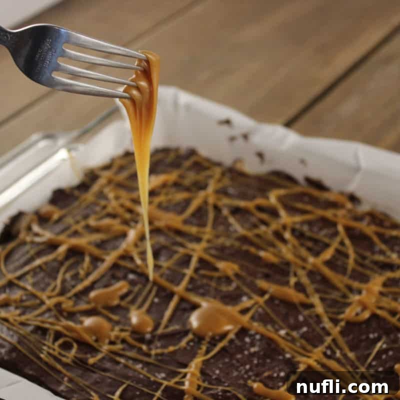 Salted Caramel Rice Krispie Treat in a parchment lined paper with a fork dripping in caramel