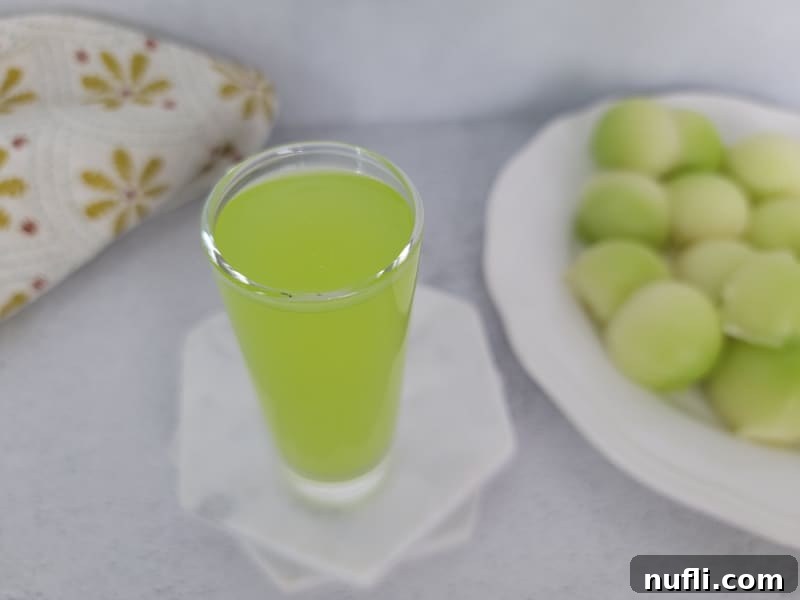 A perfectly poured Melon Ball Shot in a clear glass, presented alongside a plate of fresh melon balls for garnish.