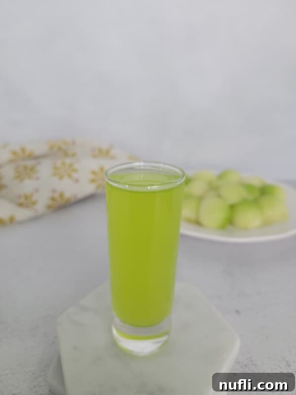 A Melon Ball Shot resting on a white coaster, accompanied by a small plate of fresh honeydew melon balls.
