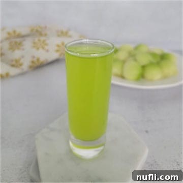 Melon Ball Shot on a white coaster next to a plate of melon