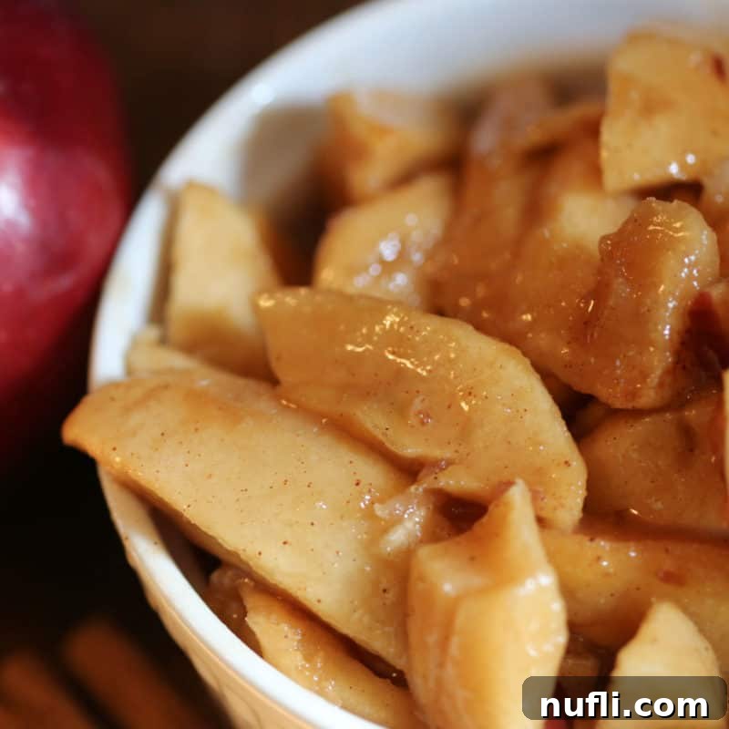 Delightful Apple Desserts Made Simple 18 Flavorful Crock Pot Fried Apples in a white bowl next to a fresh red apple and cinnamon sticks