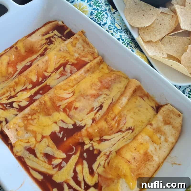 cheese enchiladas in a white casserole dish next to a bowl of tortilla chips