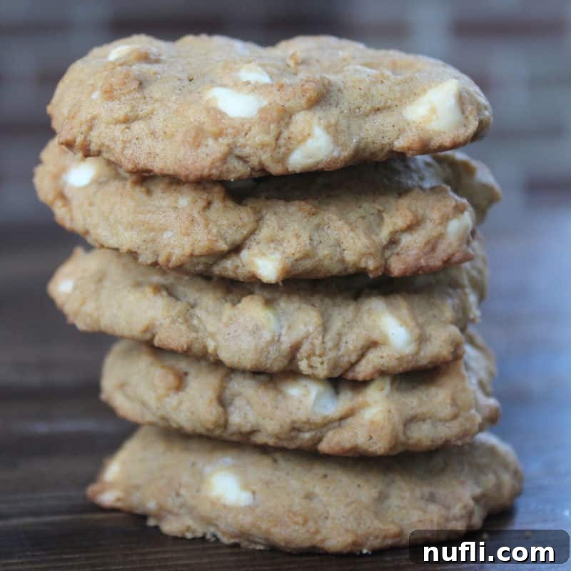 Cozy Autumn Treats You'll Love 18 A perfectly stacked pile of White Chocolate Pumpkin Spice Cookies arranged on a rustic wood board, highlighting their enticing texture and inviting aroma.