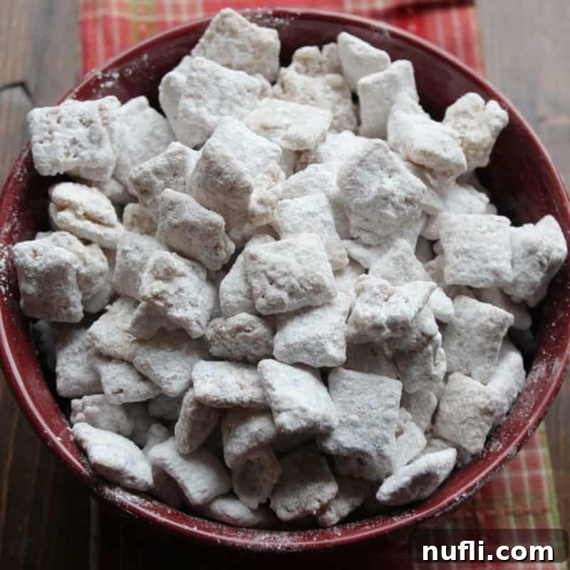 Cozy Autumn Treats You'll Love 24 Sweet and crunchy Apple Cider Muddy Buddies piled high in a burgundy bowl, set upon a rustic wood board, showcasing their powdery coating.