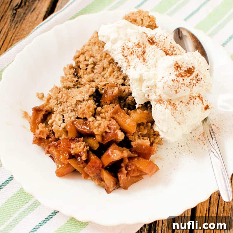 Cozy Autumn Treats You'll Love 29 A serving of warm Caramel Apple Crisp on a white plate, elegantly topped with a scoop of melting vanilla ice cream, creating a perfect balance of warm and cold.