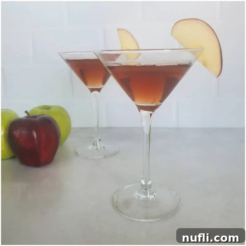 Dozens of Cozy Fall Cocktails for the Perfect Autumn 11 Two red brown martinis with apple slices in a martini glass next to green and red apples