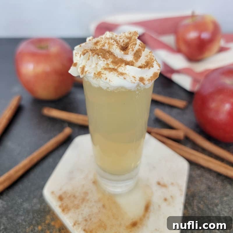 Dozens of Cozy Fall Cocktails for the Perfect Autumn 24 Apple pie shot garnished with whipped cream and cinnamon next to cinnamon sticks and red apples