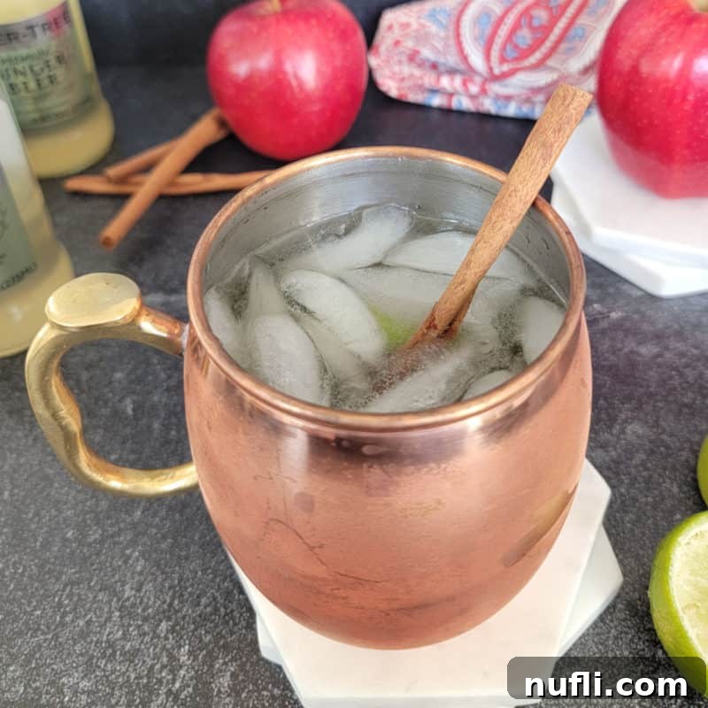 Dozens of Cozy Fall Cocktails for the Perfect Autumn 4 Apple Cider Mule in a copper mug next to apples and ginger beer