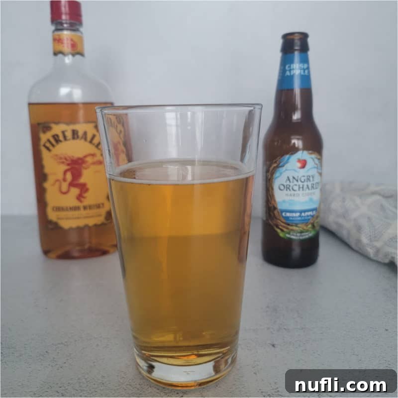 Dozens of Cozy Fall Cocktails for the Perfect Autumn 10 Angry Balls Drink in a tall glass in front of a bottle of fireball and angry orchard hard cider