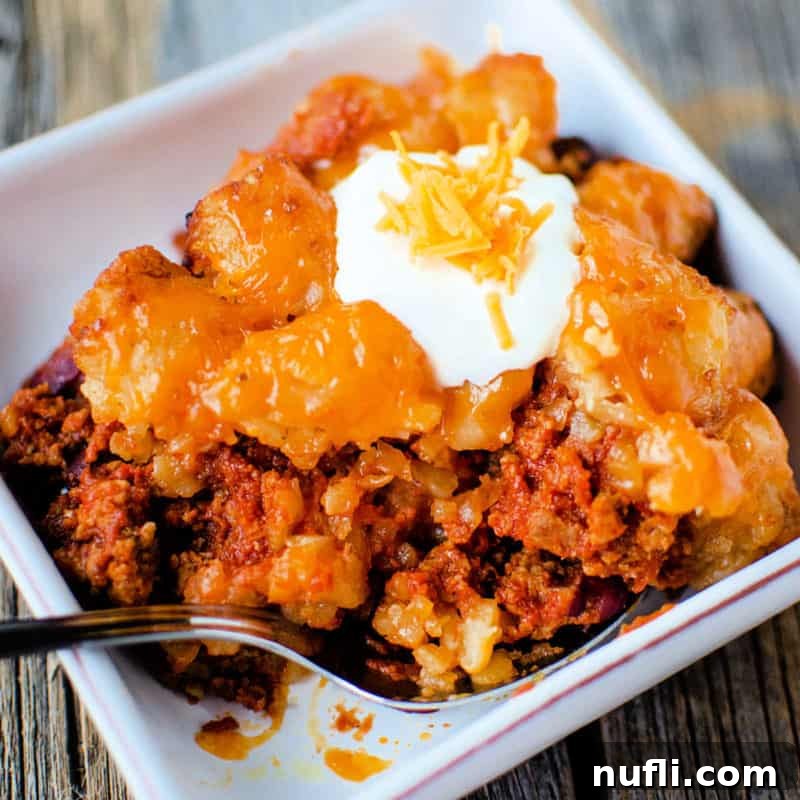 Crockpot sloppy joe tater tot casserole in a white bowl topped with sour cream and cheddar cheese