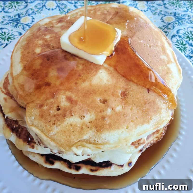 A tempting stack of Cracker Barrel pancakes on a white plate, with rich syrup generously dripping over them.