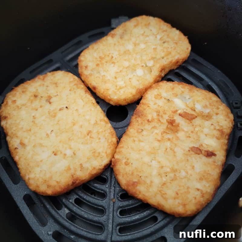 Three perfectly cooked frozen hash brown patties resting in an air fryer basket, ready to be served.