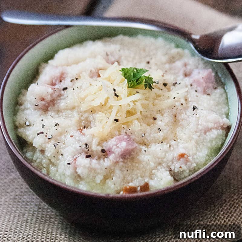 A bowl of creamy Ham and Cheese Grits with a silver spoon, highlighting its savory texture.