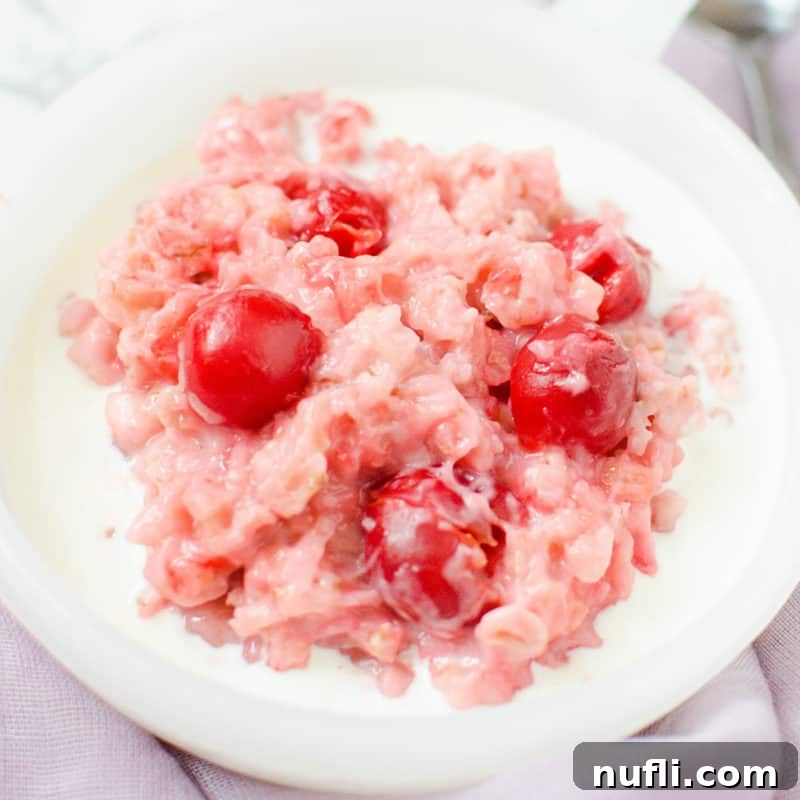 A bowl of vibrant Cherry Oatmeal with fresh cherries and cream, showcasing its appealing blush color.