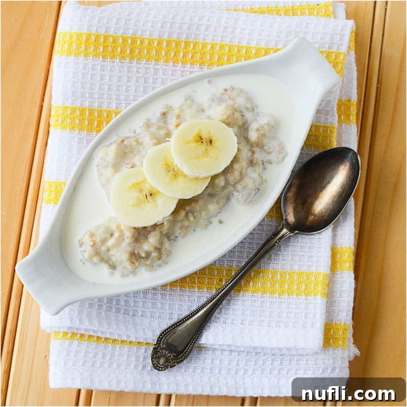 A serving of Banana Bread Oatmeal in a long bowl next to a spoon, on a white and yellow striped towel.