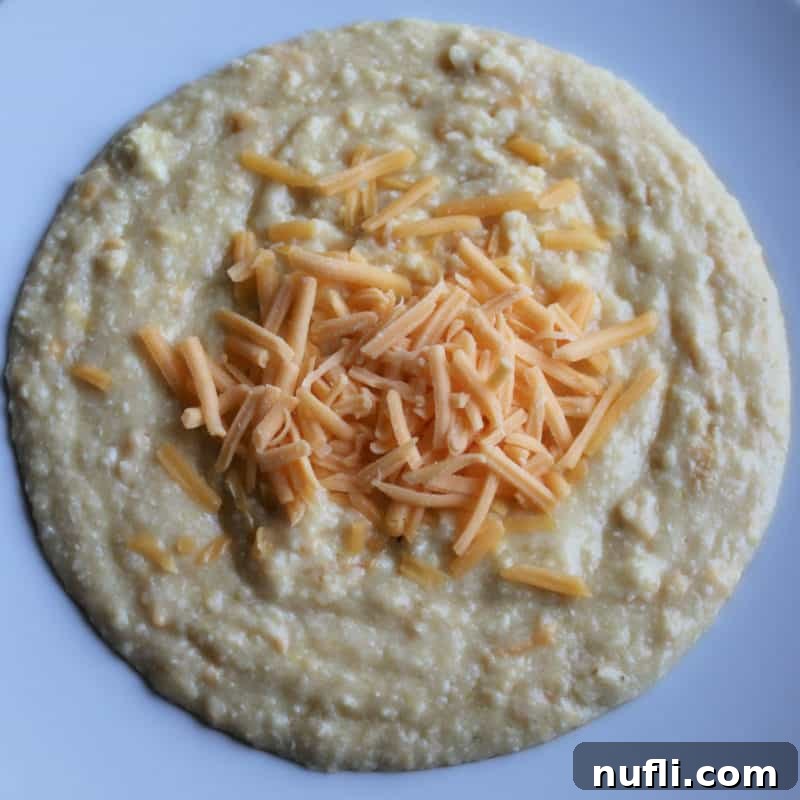 Creamy cheese grits topped with shredded cheese in a white bowl, ready to be served as a comforting meal.