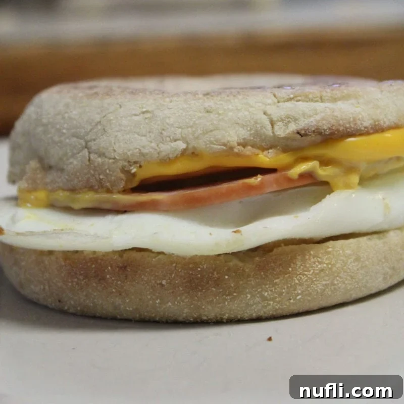 A perfect copycat Egg McMuffin with an English muffin, fried egg, slice of ham, and cheese, ready to eat.