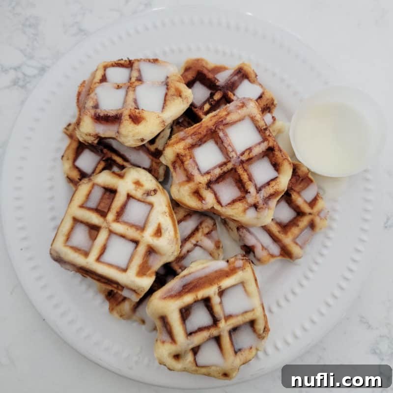 A stack of golden Cinnamon Roll Waffles covered in sweet icing on a white plate, a tempting treat for any time of day.