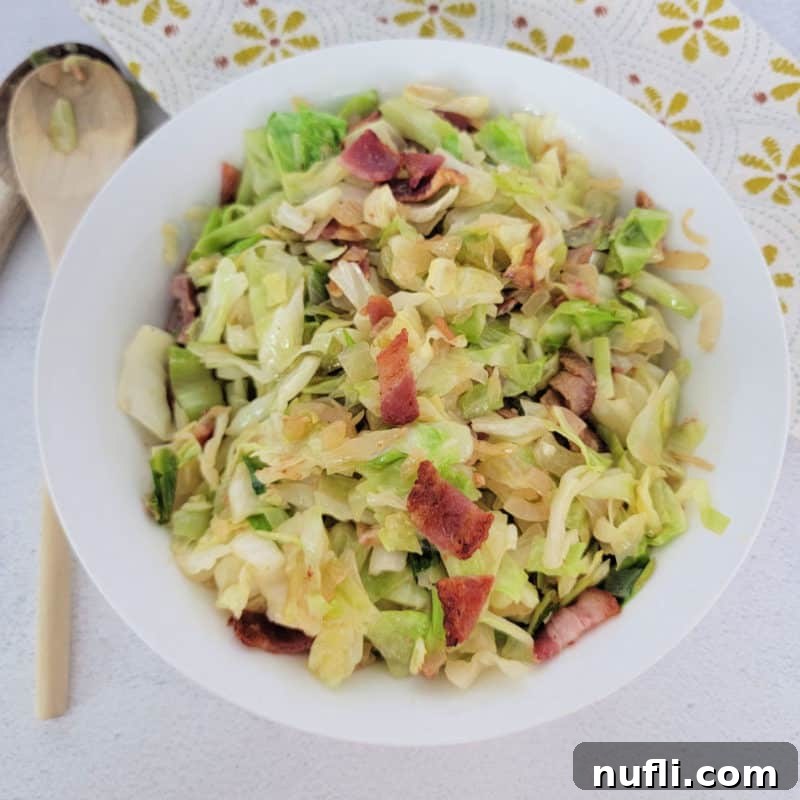southern fried cabbage with bacon in a white bowl next to a wooden spoon