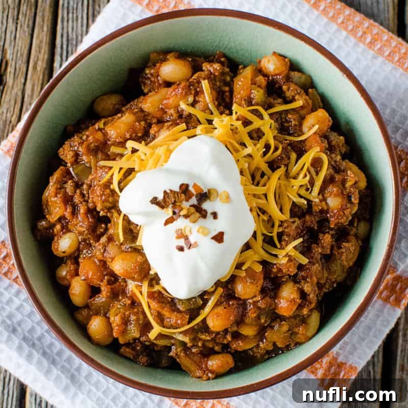 Crock Pot Spicy Bacon & Beef Chili garnished with sour cream in a bowl on a cloth napkin