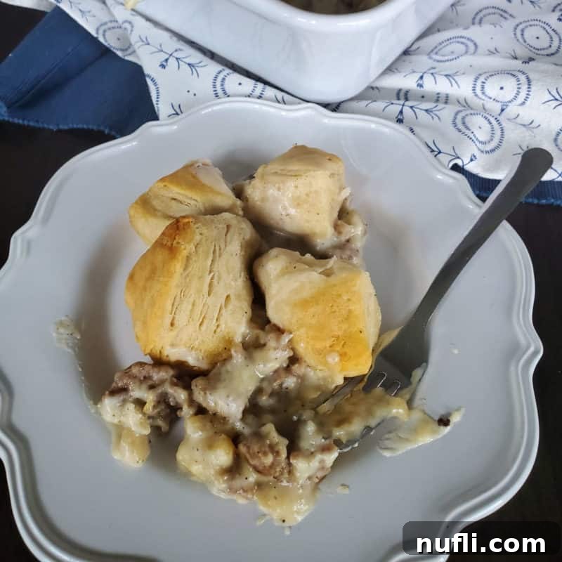 A generous serving of Sausage, Biscuit, and Gravy Casserole on a white plate, positioned near the baking dish.