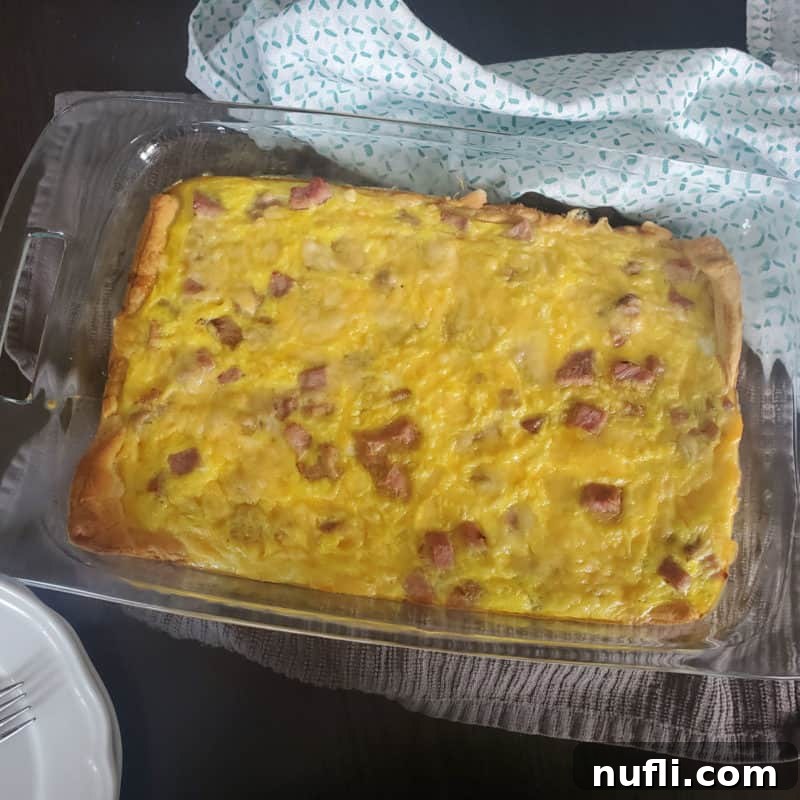 A hearty Ham, Cheese, and Egg Breakfast Casserole baked on crescent rolls, in a clear glass casserole dish.