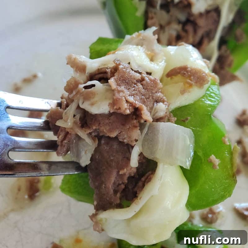 Close-up of a succulent Philly Cheesesteak Stuffed Pepper, garnished with melted cheese and fresh herbs, on a fork.