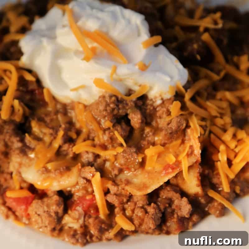 A flavorful taco beef casserole garnished with fresh cheddar cheese and a dollop of sour cream, served on a white plate.