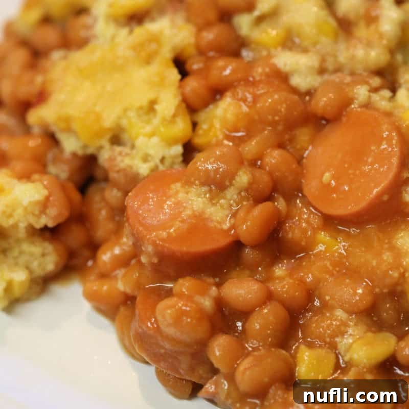 A comforting Corn Dog Casserole, served alongside baked beans, on a white plate, perfect for a family meal.