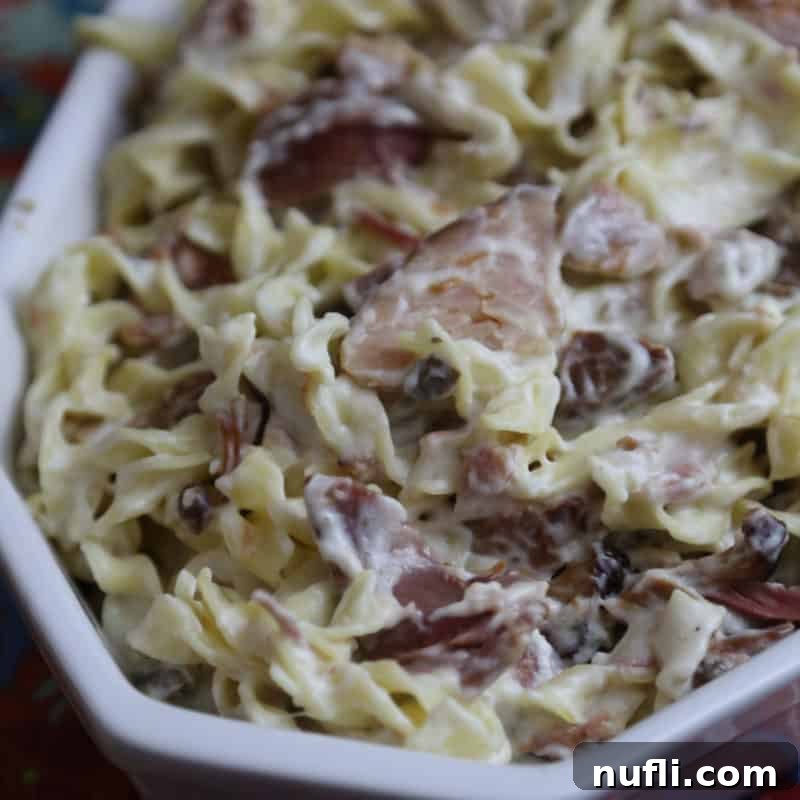 A cheesy ham and Swiss pasta casserole, rustic and comforting, served in a white casserole dish.