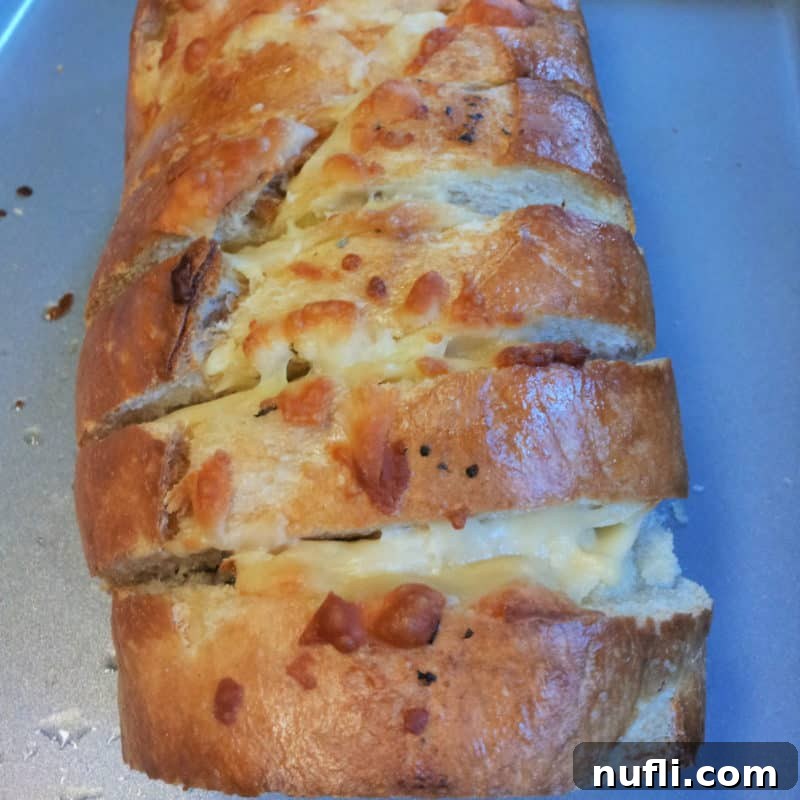 Golden-brown cheesy garlic bread, sliced and ready to pull apart, arranged on a baking sheet, showcasing its melted Parmesan and mozzarella topping.