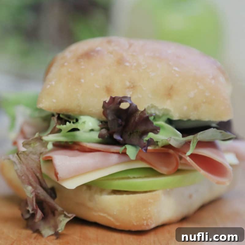A gourmet Ham and Swiss Ciabatta Sandwich with Garlic Aioli, artfully cut in half and displayed on a rustic wood board, perfect for a sophisticated lunch.