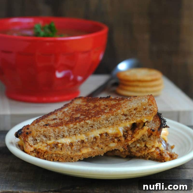 A Sloppy Joe Grilled Cheese sandwich, golden and perfectly melted, served on a white plate alongside a comforting bowl of tomato soup, ready for dipping.
