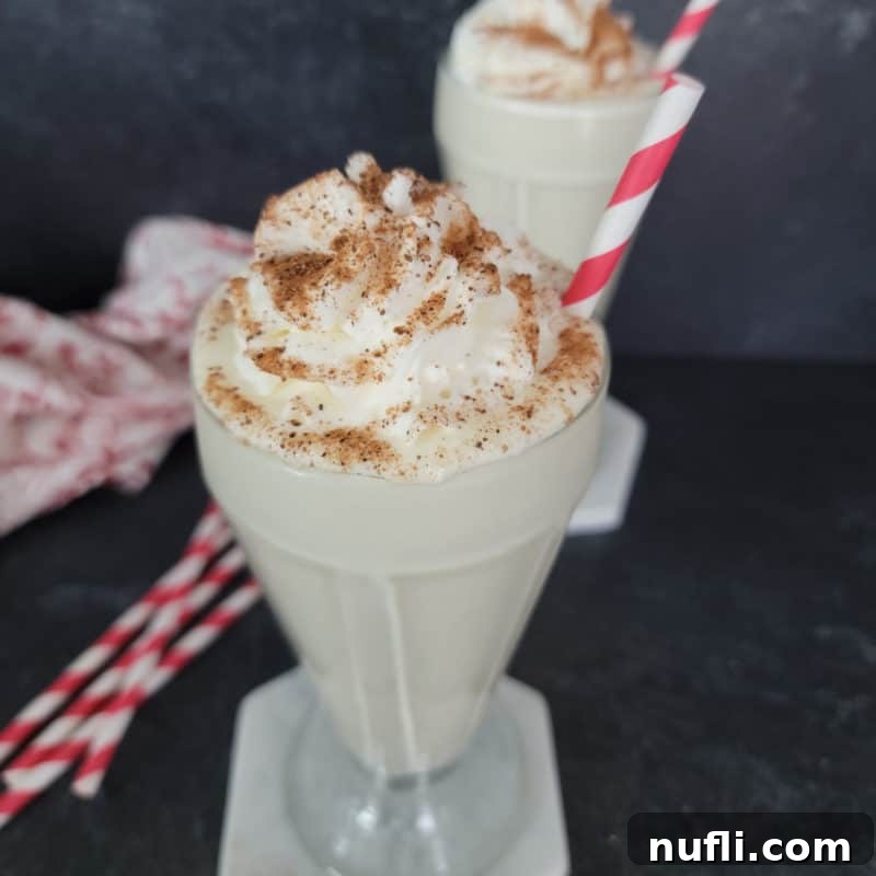 Easy Eggnog Shake served in a classic milkshake glass, garnished with a generous swirl of whipped cream and a dusting of nutmeg.