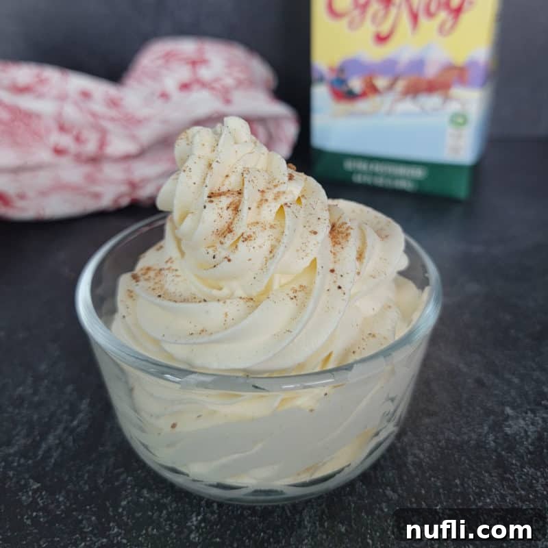 Eggnog Whipped cream beautifully swirled in a clear glass bowl, showcasing its creamy texture.