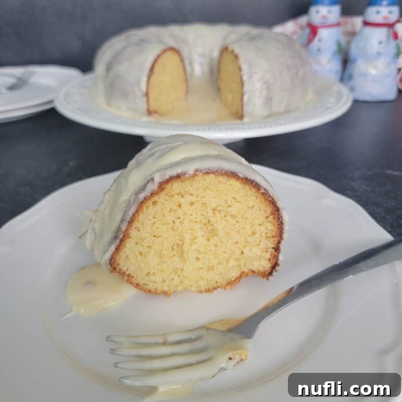 Easy Eggnog Cake with Eggnog Glaze on a white plate with a fork covered in white glaze, ready to be enjoyed.
