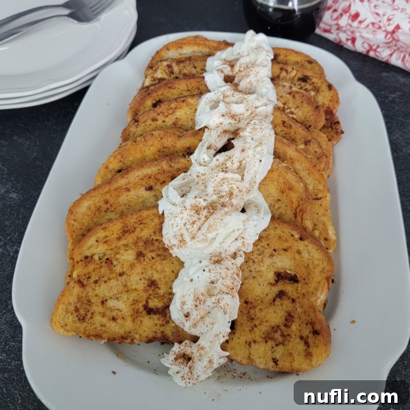 EggNog French Toast with a dollop of eggnog whipped cream, beautifully arranged on a white platter next to accompanying plates.