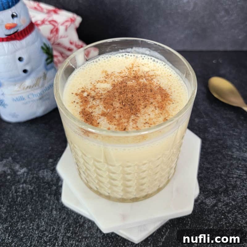Bourbon Eggnog in a crystal glass on white coasters next to a gold spoon and snowman